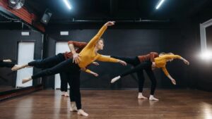 Meet You On The Mat Three people are performing a contemporary dance routine in a studio with wooden floors and black walls, embodying the energetic spirit of "Meet You On The Mat. Pilates & Dance