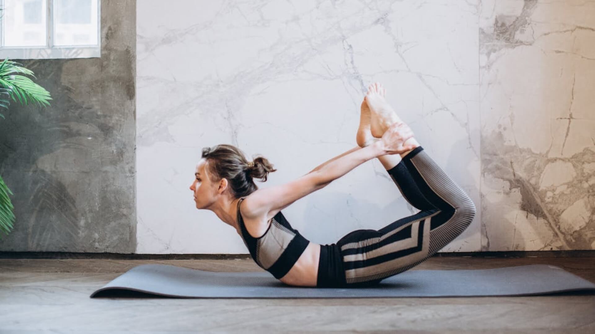 Meet You On The Mat A person performs a yoga bow pose on a gray mat in a room with a gray and white marbled wall, blending elements of Pilates to create fluidity and strength. Meet You On The Mat for an inspiring session! Pilates & Dance