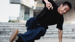 Meet You On The Mat Person in a black shirt and dark pants energetically performing a breakdancing move on a concrete surface with a building in the background, showcasing incredible dance skills. Pilates & Dance