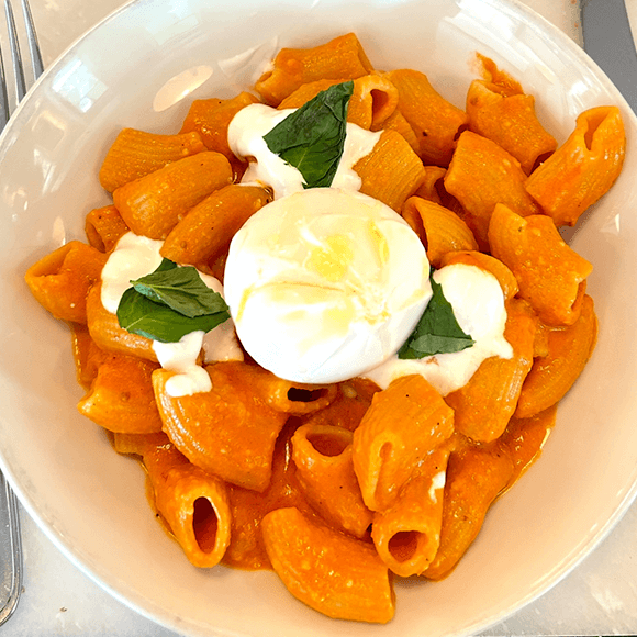 Meet You On The Mat A bowl of rigatoni pasta in creamy orange sauce, topped with a ball of burrata cheese, fresh basil leaves, and a drizzle of olive oil. Pilates & Dance